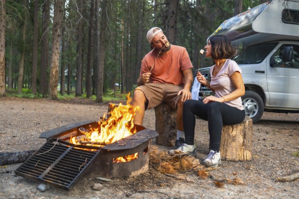 Tourists roasting marshmallows in a campfire near their campervan, enjoying a relaxing evening in the woods of banff national park in the canadian rockies, alberta