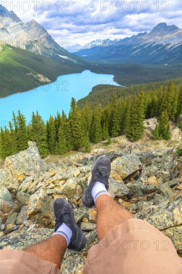 Hiker resting on a rocky mountain top, soaking in the stunning panoramic view of turquoise peyto lake and the majestic canadian rockies in banff national park