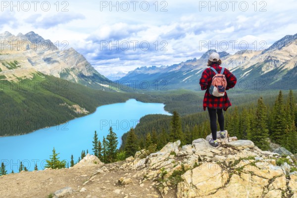 Female hiker standing on a rocky cliff, gazing at the turquoise waters of peyto lake and the surrounding mountains in banff national park, alberta, on a cloudy day