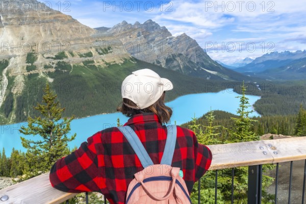 Female tourist with backpack and baseball cap enjoying breathtaking panoramic view of turquoise peyto lake and surrounding canadian rockies in banff national park. Alberta. Canada. During summer day