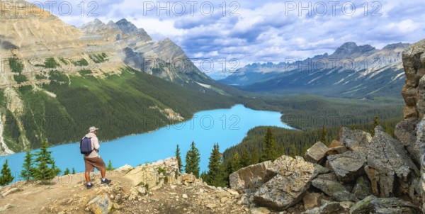 Tourist with backpack is enjoying the breathtaking panoramic view of the turquoise peyto lake and surrounding canadian rockies in banff national park, alberta, under a cloudy sky