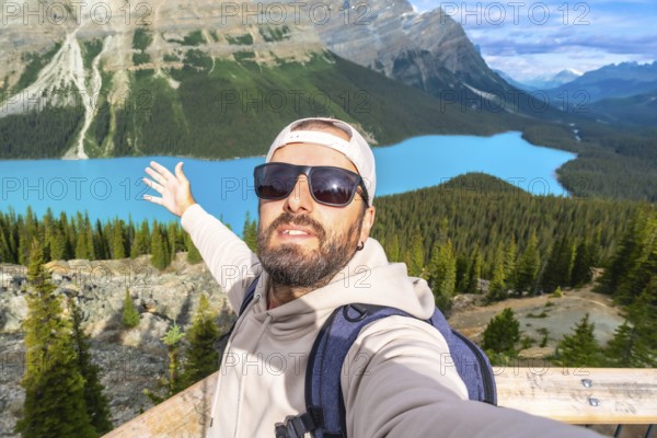Tourist with a backpack and sunglasses taking a selfie at the scenic viewpoint of peyto lake in banff national park, enjoying the stunning turquoise waters and mountains