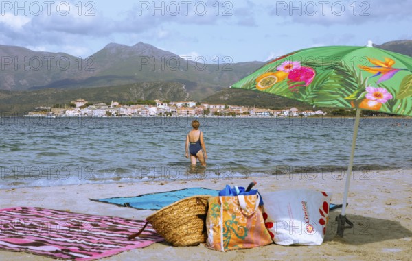 Sunshade and swimwear blurred on the beach or Plage de la Roya, in the back Saint-Florent on the Gulf of Saint-Florent in the Mediterranean, Haute-Corse, Corsica