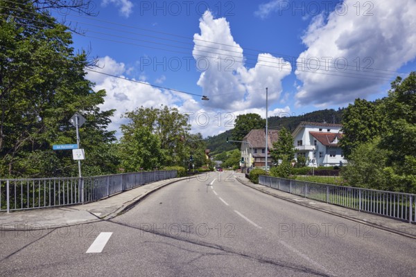 Car bridge and footbridge, metal railings, general architecture, houses, sidewalk, road, lanes, traffic lights, hills, hilly landscape, coniferous forest, trees, blue sky, cumulus clouds, intersection An der Niederbruck, Am Martinshof and Untertalstraße, Simonswald, Black Forest, Emmendingen district, Baden-Württemberg, Germany