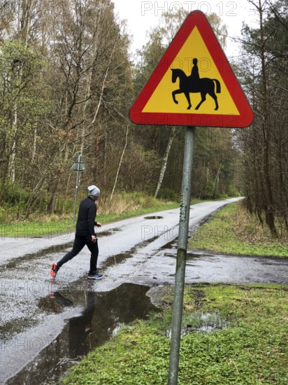 Person jogging on wet forest road with road sign for riding on horse in Ystad, Skåne County, Sweden, Scandinavia