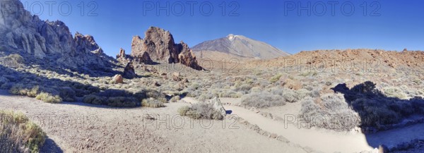 Barren rocky landscape with blue sky, dry vegetation and impressive Pico del Teide in the background, La Orotava Tenerife