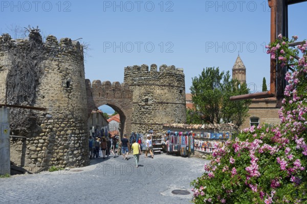 An old city gate with fortress wall and tower, animated by tourists, flanked by colorful stalls and flowers, city gate, entrance to the old town, Sighnaghi, Signagi, Kakheti province, Greater Caucasus, Georgia, Western Asia