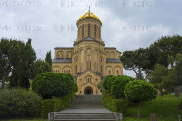 A magnificent church with a golden dome and symmetrical steps surrounded by lush greenery, Sameba Cathedral, Trinity Cathedral, Tbilisi, Tbilisi, Georgia