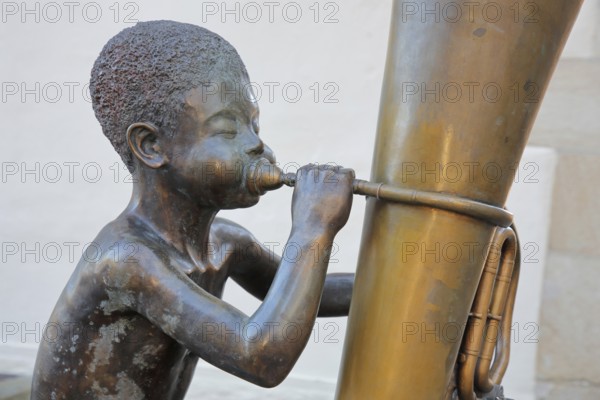 Sculpture boy with tuba by Guido Messer 1991, modern art, bronze sculpture, playing music, tuba, brass instrument, sitting, jack, big cheeks, bubbles, size comparison, big, small, half-timbered house, music school, Waldenbuch, Baden-Württemberg, Germany