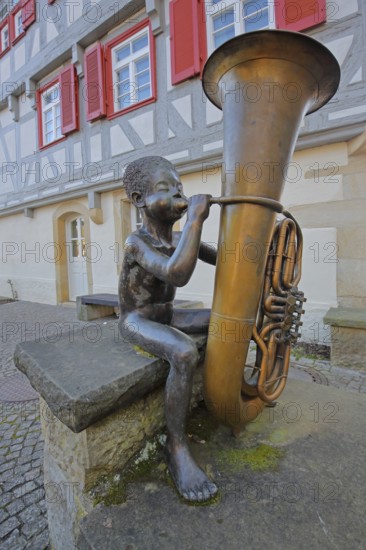 Sculpture boy with tuba by Guido Messer 1991, modern art, bronze sculpture, playing music, tuba, brass instrument, sitting, jack, size comparison, big, small, big cheeks, blowing, half-timbered house, music school, Waldenbuch, Baden-Württemberg, Germany