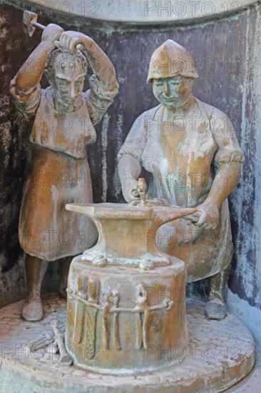 Blacksmith working metal on an anvil at the guild fountain by Bonifatius Stirnberg 1983, modern art, bronze sculpture, city history, historical profession, craftsman, processing, manufacturing, forging, hammering, hammer, steel, metal, metalworking, tools, guild fountain, Reutlingen, Swabian Jura, Baden-Württemberg, Germany