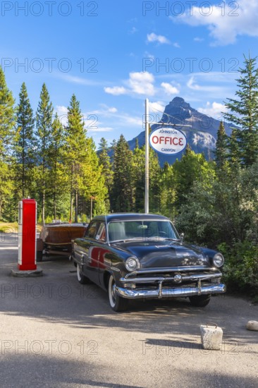 Classic car with a wooden boat parked in front of the johnston canyon office sign, with castle mountain in the background, in banff national park, alberta, canada, on a clear summer day