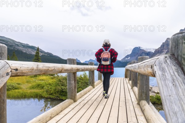 Female tourist walking on a wooden bridge enjoying the breathtaking view of bow lake and surrounding mountains in banff national park, a beautiful natural landscape in the canadian rockies
