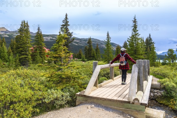 Tourist standing on a wooden bridge, admiring the breathtaking view of bow lake and surrounding mountains in banff national park, alberta, canada, with a red lodge among the trees