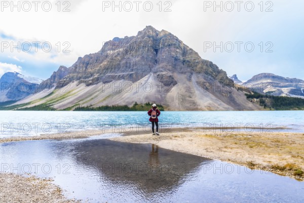 Female hiker stands at the edge of bow lake, admiring the turquoise water and imposing mountain backdrop in banff national park, alberta, canada, a breathtaking scene of nature's grandeur
