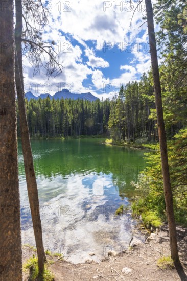 Emerald green waters of herbert lake reflecting a cloudy blue sky and surrounding pine forest with rocky mountains in the background, banff national park, alberta, canada