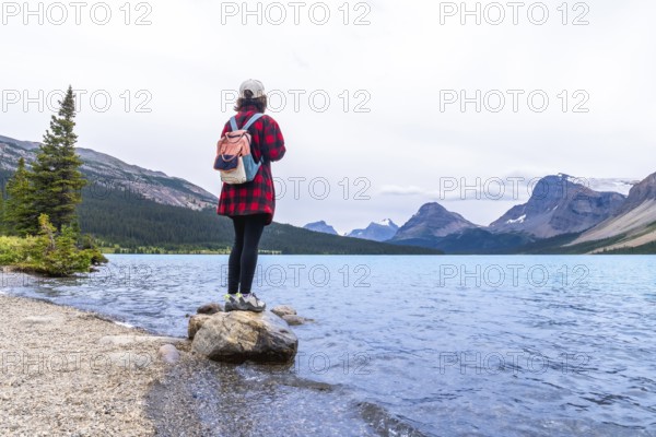 Female tourist standing on a rock at bow lake, admiring the turquoise waters and majestic mountains of banff national park on a serene summer day