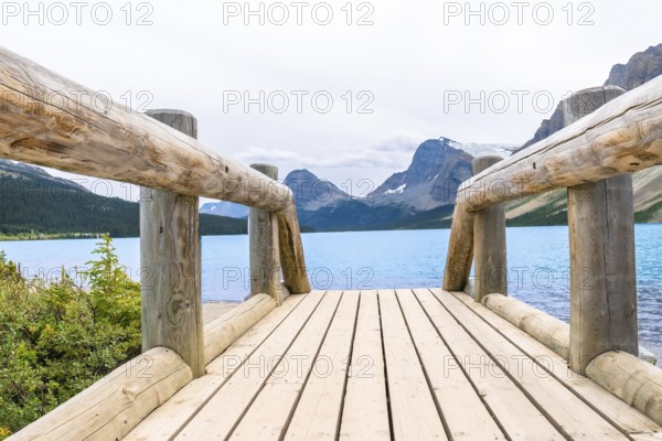 Wooden bridge leading to turquoise waters of bow lake, framed by the majestic canadian rockies in banff national park, embodies the area's natural beauty and tranquility