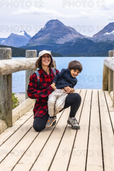Mother happily holds her son on a wooden bridge, enjoying the stunning turquoise waters of bow lake and the majestic mountains of banff national park in the canadian rockies