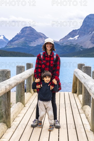 Smiling mother and son embracing the stunning scenery of turquoise bow lake and surrounding mountains in banff national park, capturing a beautiful family moment in nature