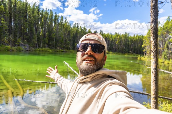 Happy tourist taking a selfie with outstretched arms, embracing the stunning turquoise waters of herbert lake, surrounded by lush pine forests and blue skies in banff national park