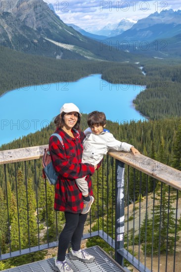 Mother holding her son while admiring the stunning panoramic view of vibrant turquoise waters at peyto lake in banff national park, surrounded by majestic mountains