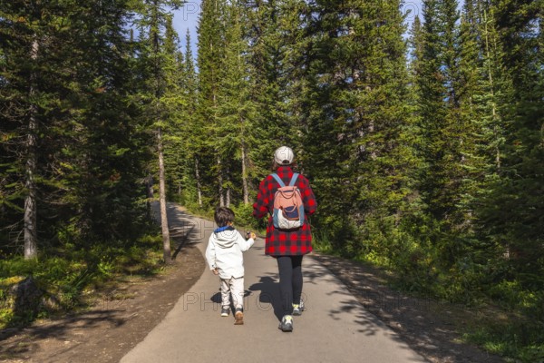 Mother and child holding hands, enjoying a leisurely hike along a paved path, surrounded by the lush green trees of banff national park in the canadian rockies