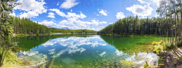Breathtaking panoramic view of pristine herbert lake reflecting a vibrant blue sky with fluffy clouds, surrounded by lush green forests in banff national park, alberta