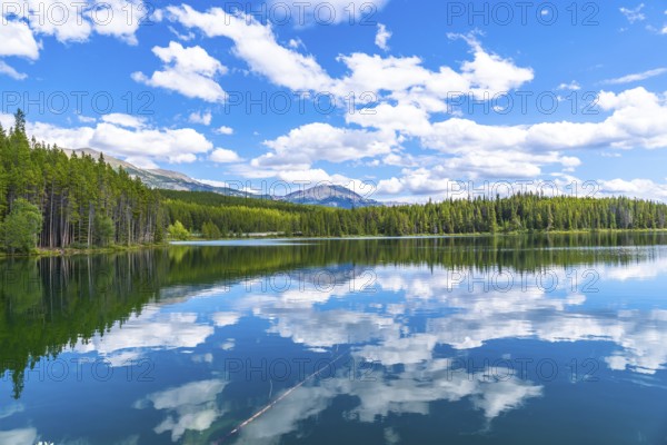 Calm waters reflecting a stunning cloudy sky over herbert lake, surrounded by lush pine forests and majestic mountains in banff national park