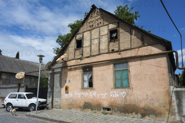 A dilapidated house with leaning antennas and graffiti, next to a parked car under cloudy sky, traditional German residential building, Nikolaistraße 38-40, Bolnissi, Katharinenfeld, founded by Caucasian German settlers, Lower Kartli region, Kwemo Kartli, Georgia