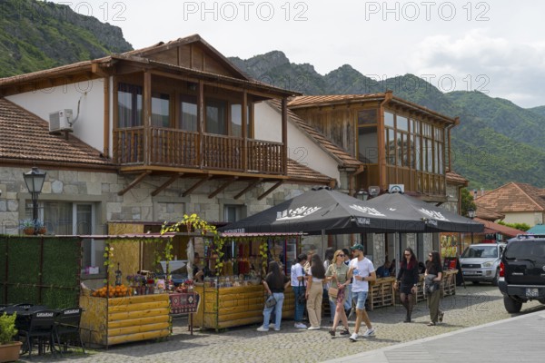 Tourists discover market stalls in front of traditional wooden buildings in mountainous surroundings, Mtskheta, Mtskheta, Mtskheta-Mtianeti region, Georgia