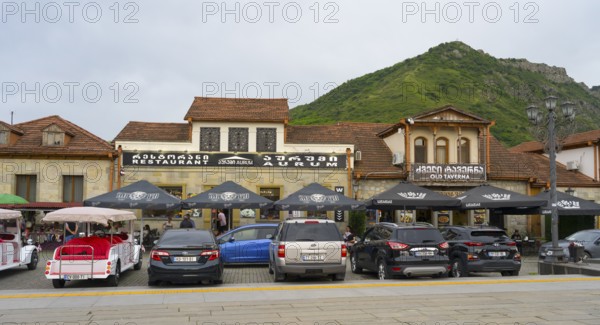 Street scene with cars parked in front of a restaurant with mountain backdrop in the background, Mtskheta, Mtskheta Square, Mtskheta, Mtskheta-Mtianeti region, Georgia