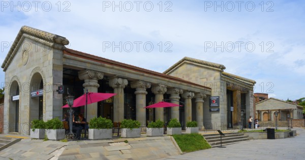 Historic stone building with ancient columns and red umbrellas under cloudy sky, Mtskheta, Mtskheta, Mtskheta-Mtianeti region, Georgia