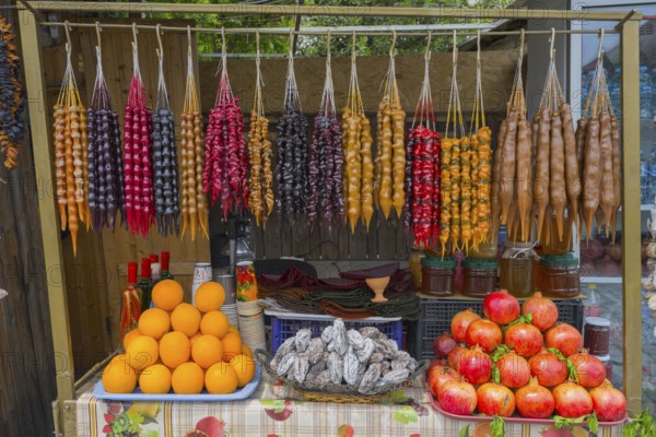 Colourful fruit and candy display with hanging goodies, Churchkhela, Georgian confections, 'Georgian Snickers', in front oranges, dried fruits and pomegranates, Mtskheta, Mtskheta, Mtskheta, Mtskheta, Mtskheta-Mtianeti region, Georgia
