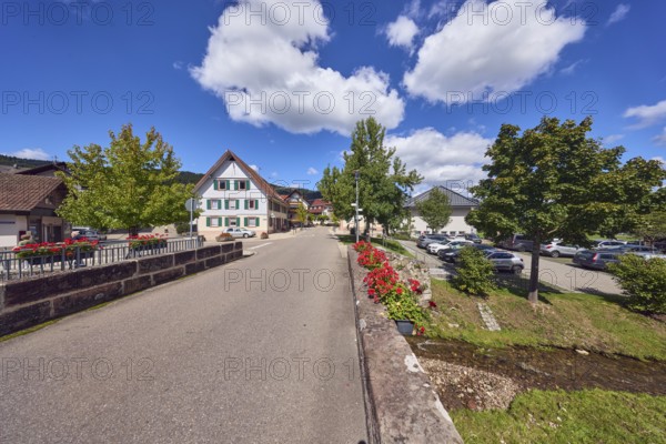 Car bridge and pedestrian bridge, Hofstetterbach stream, sandstone, flower boxes, zonal geranium (Pelargonium hortorum), general architecture, buildings, houses, trees, meadow, hill, coniferous forest, car park with cars, blue sky, cumulus clouds, intersection main road with Unterdorf, Hofstetten, Black Forest, Ortenaukreis, Baden-Württemberg, Germany