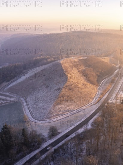 Aerial view of a hill in morning light with snow-covered roads and surrounding forest, future PV construction on old deposit, Lindenrain industrial park, Calw, Germany