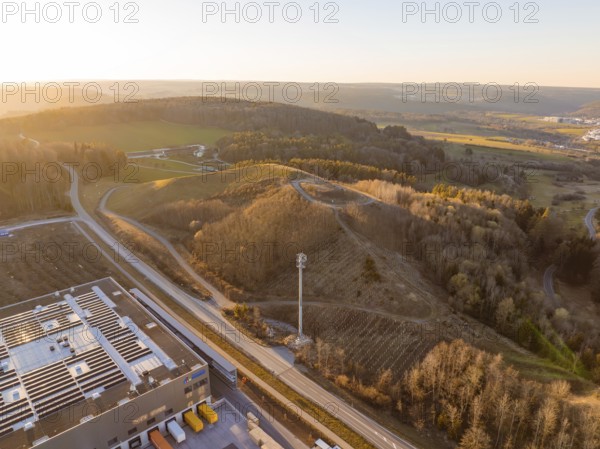 Telecommunication tower over hilly landscape and industrial buildings in the evening light, future PV construction on old deposit, Lindenrain industrial park, Calw, Germany