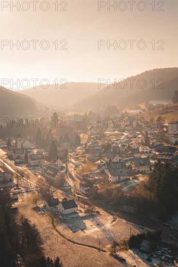Aerial view of a snowy village in a valley at sunset with surrounding forests and hills, Enzklösterle, Calw district, Germany