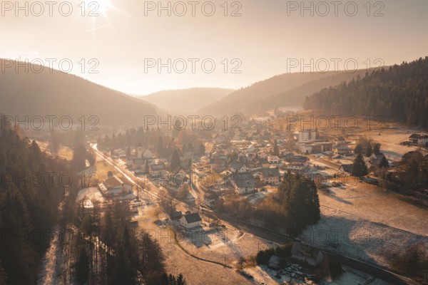 Aerial view of a village surrounded by snow-covered forests and mountains in the evening sun, Enzklösterle, Calw district, Germany
