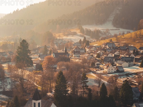 Snowy village in a valley surrounded by rolling hills and forest in warm evening light, Enzklösterle, Calw district, Germany
