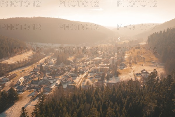 Panoramic view of a village with snow-covered roofs surrounded by forests and hills in the evening light, Enzklösterle, Calw district, Germany
