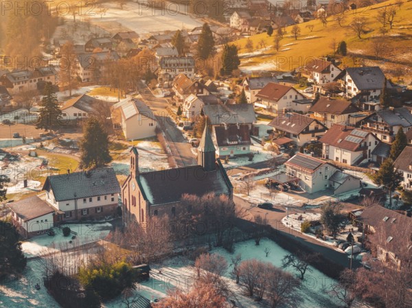 Village in winter with a central church surrounded by houses, hills and soft, warm light, Enzklösterle, Calw district, Germany
