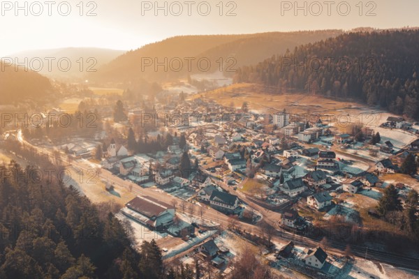 Extensive aerial view of a valley with snowy houses surrounded by mountains and warm sunset light, Enzklösterle, Calw district, Germany