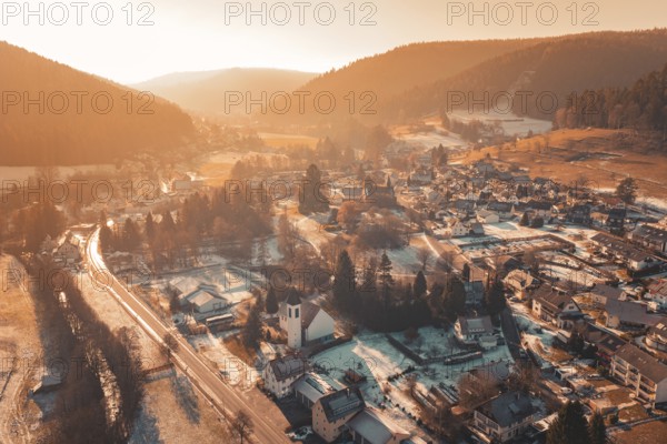 Snowy village from above, surrounded by mountains and illuminated by the warm atmosphere of sunset, Enzklösterle, Calw district, Germany