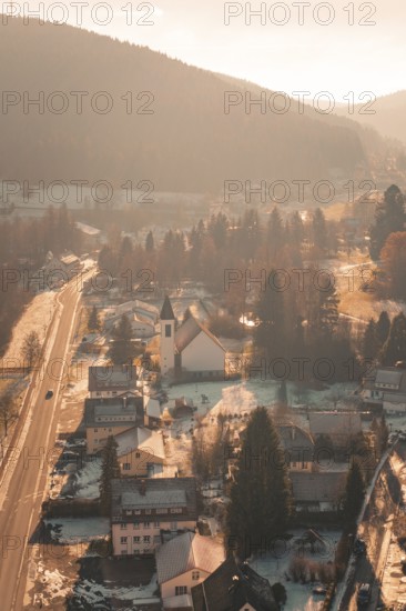 View of a village road with snowy houses and a church in the evening light, Enzklösterle, Calw district, Germany