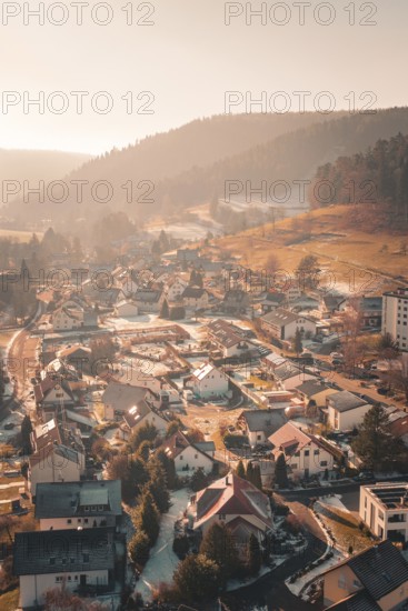 An airy panorama of a village surrounded by wintry hills in warm sunlight, Enzklösterle, Calw district, Germany