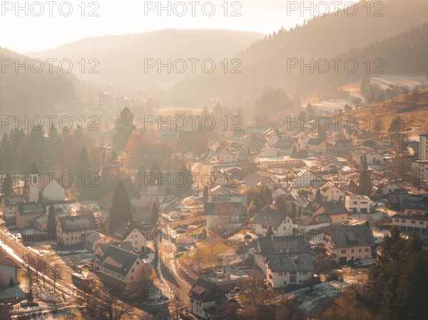 A picturesque village is situated in a valley surrounded by hilly forests and gentle autumn fog, Enzklösterle, Calw district, Germany