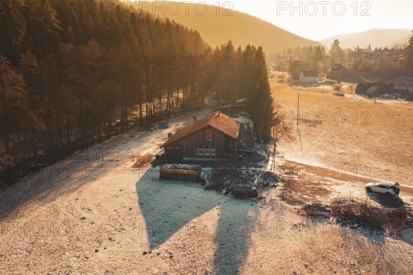Wooden house surrounded by snow, nestled between meadow and forest in warm sunset light, Enzklösterle, Calw district, Germany