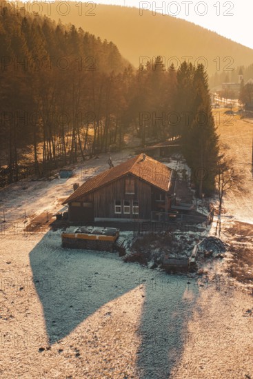 Wooden house on the edge of a forest whose shadows are cast in the snow by warm sunset light, Enzklösterle, Calw district, Germany