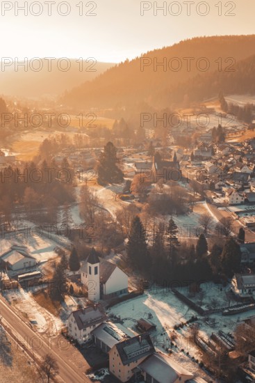 Picturesque image of a snowy village in a valley surrounded by mountains in warm sunlight, Enzklösterle, Calw district, Germany